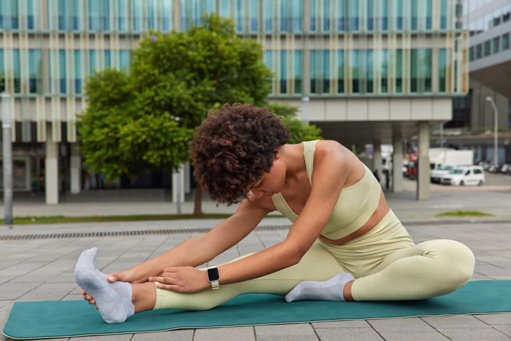 Woman stretching her leg and foot outdoors on an exercise mat.